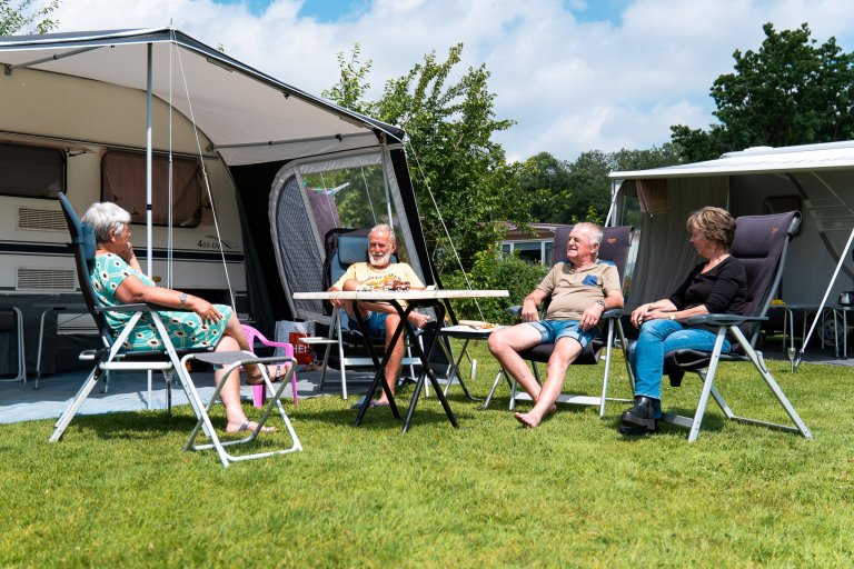 Een groep mensen zit voor een caravan met voortent rondom een tafel